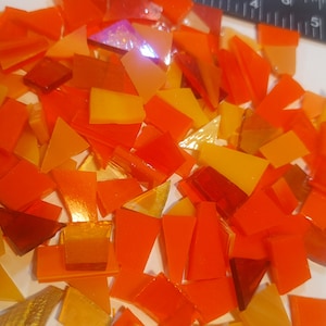 May include: A pile of orange, yellow, and red glass mosaic tiles. The tiles are in various shapes and sizes, including squares, rectangles, and triangles.