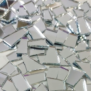 May include: A collection of small, irregularly shaped silver mirror glass pieces with reflective surfaces. These fragments feature various geometric forms, including trapezoids, triangles, and rectangles, with smooth edges and a clear, metallic finish.