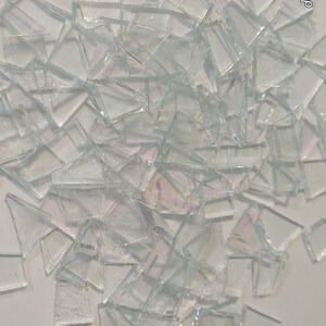 Puede incluir: Una colecci&oacute;n de fragmentos de vidrio transparente de forma irregular, con superficies iridiscentes. Las piezas est&aacute;n dispersas sobre un fondo blanco, creando una exhibici&oacute;n texturizada y reflectante. Los fragmentos var&iacute;an en tama&ntilde;o y forma, capturando la luz para producir un sutil efecto arco&iacute;ris.