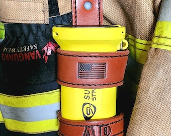 May include: A yellow flashlight with a brown leather holster. The holster features an American flag design and the text "SU STR" and "AID". The flashlight is attached to a black clip.