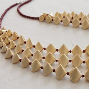 Peut inclure: Un collier multi-rangs composé de perles beiges de forme triangulaire reliées par un cordon marron.