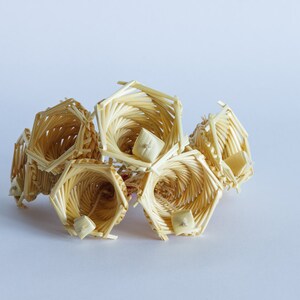 May include: A cluster of woven straw bells, each with a distinctive shape and texture. The bells are a light beige colour and have a natural, rustic appearance.