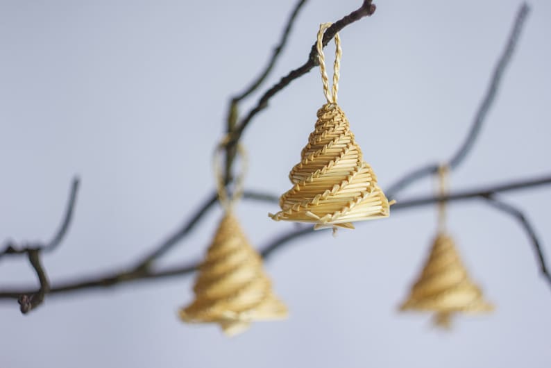 May include: Three straw Christmas tree decorations hanging from bare branches. The decorations are made of woven straw and are a light brown colour.