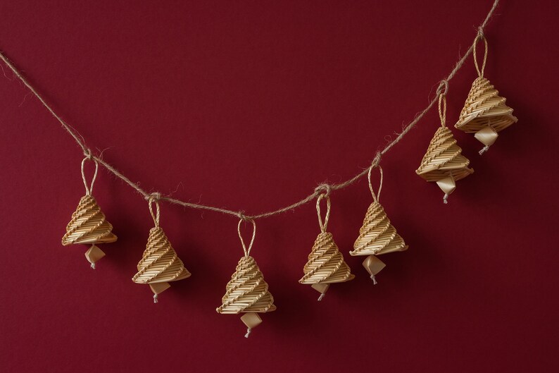 May include: A string of seven small, woven, beige Christmas tree decorations hanging on a red background.