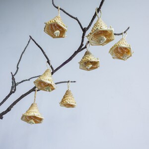 May include: A collection of eight woven straw ornaments hanging from a bare branch. The ornaments are shaped like bells and are a light beige colour.