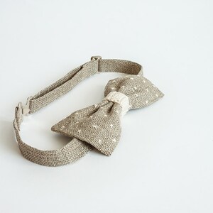 May include: A tan bow tie with a white dotted pattern and a cream-colored center. The adjustable neckband is made of the same tan fabric. The bow tie is a classic accessory for formal or semi-formal attire.