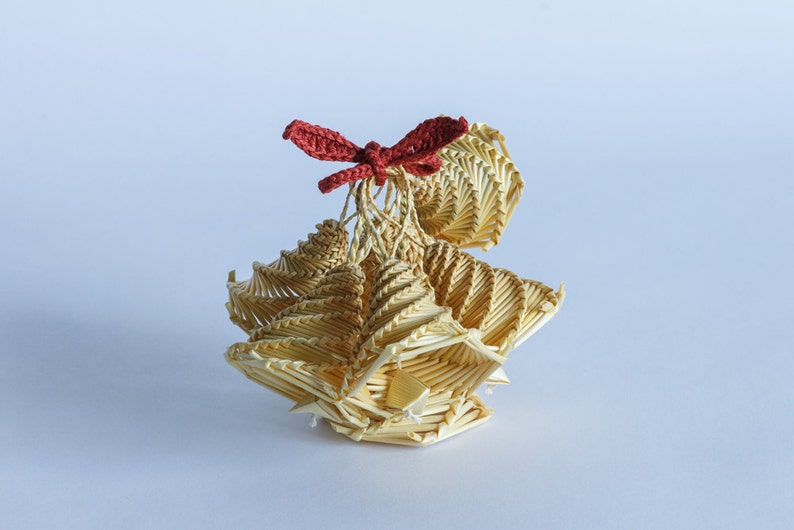 May include: A small, intricately woven straw ornament with a red crocheted bow on top. The ornament is shaped like a bell or a flower.
