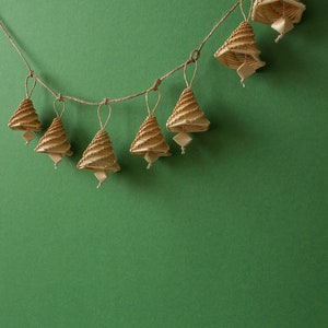 May include: A string of seven small, woven, brown, bell-shaped ornaments hanging from a twine string against a green background.