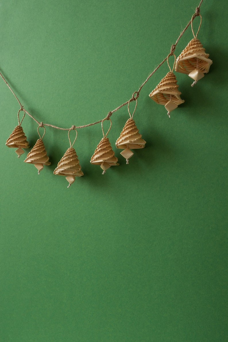May include: A string of seven small, woven, brown, bell-shaped ornaments hanging from a twine string against a green background.