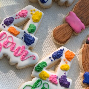 May include: Two decorated sugar cookies with the number four and the word "four" written in green icing. The cookies are decorated with colourful paint splatters.