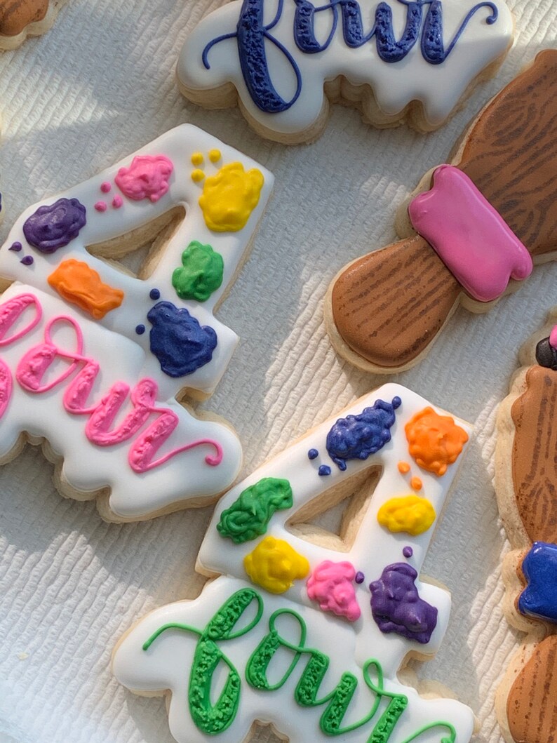 May include: Two decorated sugar cookies with the number four and the word "four" written in green icing. The cookies are decorated with colourful paint splatters.