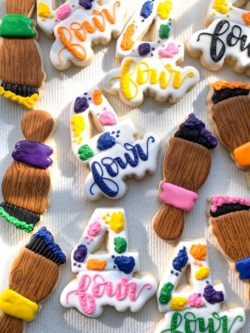 May include: A set of nine decorated sugar cookies featuring the number four and the word "four" in various colours and styles. The cookies are decorated with paint splatters and paintbrushes.