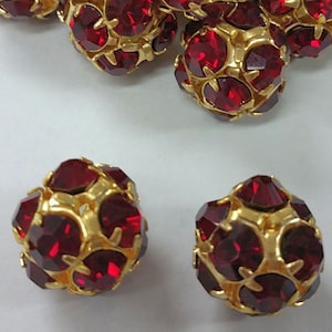 May include: Red rhinestone beads with gold accents. The beads are round and have a faceted design.