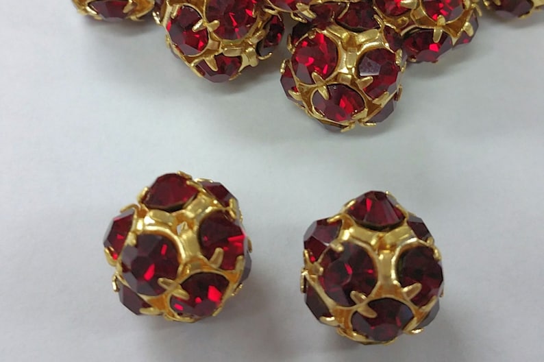 May include: Red rhinestone beads with gold accents. The beads are round and have a faceted design.