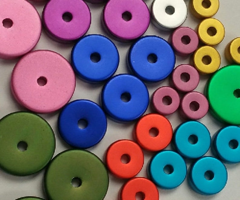 May include: Assortment of colorful round wooden buttons with different colors, including pink, blue, green, red, and gold. The buttons have a hole in the center.
