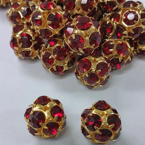 May include: A group of red and gold round beads with a faceted design. Two beads are separated from the group and are in focus.