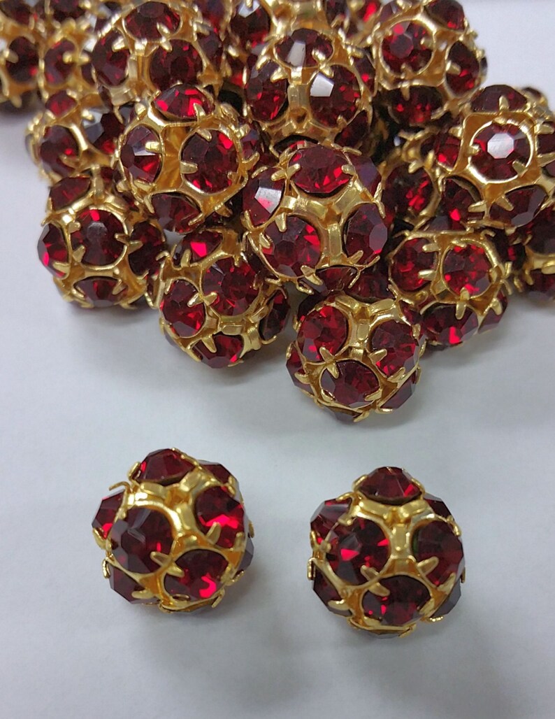 May include: A group of red and gold round beads with a faceted design. Two beads are separated from the group and are in focus.