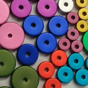 May include: Assortment of colorful round wooden buttons with different colors, including pink, blue, green, red, and gold. The buttons have a hole in the center.