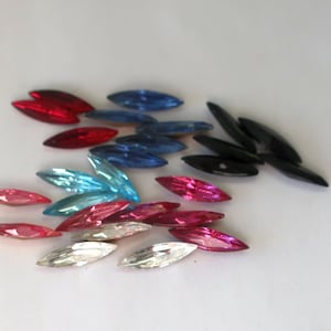 May include: A collection of colorful, oval-shaped rhinestones in various colors, including red, blue, pink, and black. These decorative embellishments are ideal for crafts and adding sparkle to projects.