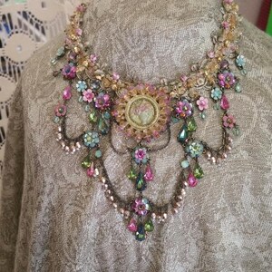 May include: A multi-layered necklace featuring pink, green and gold beads, with a cameo pendant. The necklace is made of metal and has a vintage style.
