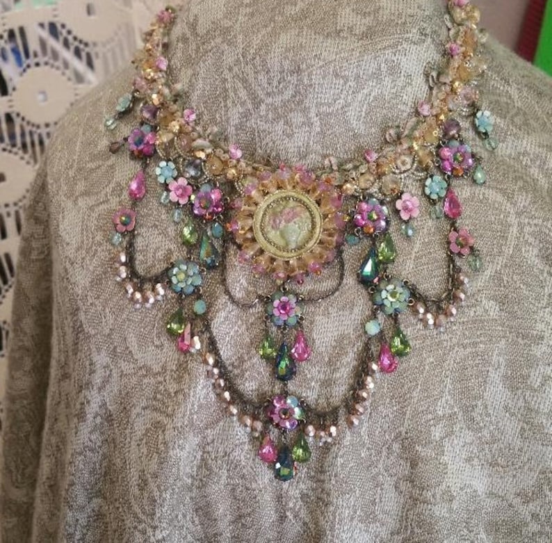 May include: A multi-layered necklace featuring pink, green and gold beads, with a cameo pendant. The necklace is made of metal and has a vintage style.