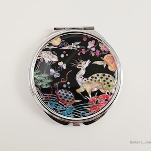 May include: A silver compact mirror with a black background and a colorful design featuring a deer, flowers, and a turtle. The design is made of mother of pearl.