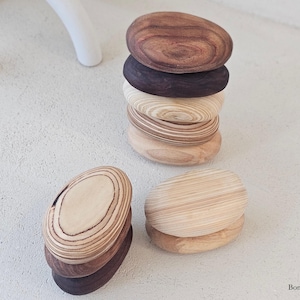 May include: A stack of wooden, oval-shaped stones in varying shades of brown and tan. The stones are arranged in a tower, with two additional stacks nearby. The wood grain is visible, adding texture to the natural decor.