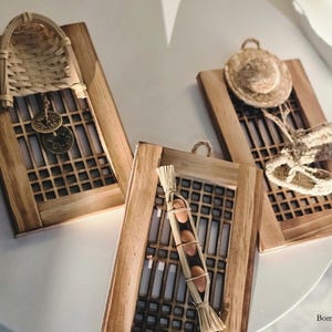 May include: Three wooden frames with intricate latticework designs. Each frame features a different natural element: a woven basket, a straw hat, and a bundle of dried grass with small brown objects.