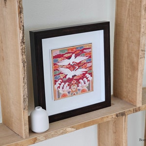 May include: A framed artwork with a red, white, and blue design featuring two white birds in flight. The artwork is displayed on a wooden shelf with two small white vases.