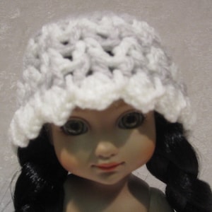 May include: A doll wearing a white and gray crocheted hat with a scalloped edge. The doll has long black hair and blue eyes.