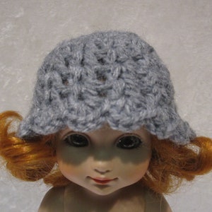 May include: A gray crocheted hat with a flower pattern. The hat is worn by a doll with red hair.
