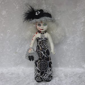 May include: A handmade doll with a black and silver spiderweb print dress, a gray and black hat with a feather, and a matching purse. The doll has white hair, green eyes, and makeup to resemble a zombie.