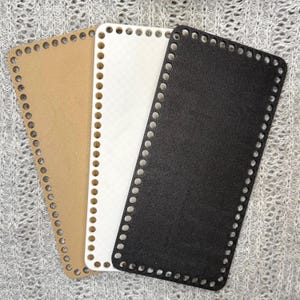May include: Three rectangular bases for crochet or knitting projects, each featuring rounded corners and a series of evenly spaced holes along the perimeter. The bases are colored in tan, white, and black, providing a sturdy foundation for bags.
