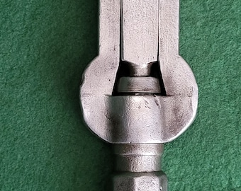Puede incluir: Una llave inglesa de plata con una superficie texturizada. La llave tiene un mango fijo y una mordaza móvil.
