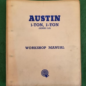 May include: A tan-colored workshop manual for the Austin 1-ton and 1 1/2-ton trucks, series LD. The cover features the text "AUSTIN 1-TON, 1 1/2-TON (SERIES LD) WORKSHOP MANUAL" in blue lettering and a blue and white BMC logo.