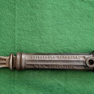May include: A vintage Bridgeport Hardware tool with a red handle. The metal tool has a curved claw on one end and a cutting edge on the other. The tool is marked "Bridgeport Hardware" and "M.R.C. Corporation."