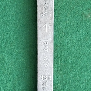 May include: A silver wrench with a 9/16 inch size marked on it. The wrench also has markings for 5/8, 3/8, and 1/2 inch sizes. The wrench is marked "BSW" and "1947".
