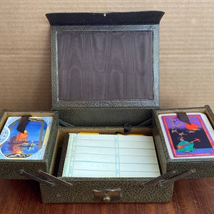 May include: A green leather box with two compartments, each containing a deck of cards. The top compartment has a brown fabric lining. The box has a metal latch and hinges.