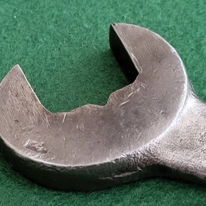 K&ouml;nnte beinhalten: Nahaufnahme eines silbernen Schraubenschl&uuml;ssels mit abgerundetem Kopf und leicht abgenutzter Oberfl&auml;che.