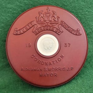 Könnte beinhalten: Runde, rotbraune Krönungsmedaille vom County Borough of Doncaster, mit Text und einem zentralen weißen Cameo mit zwei Profilen. Die Medaille enthält die Jahreszahlen 19 und 37 sowie den Namen Alderman S. Morris J.P. Mayor.