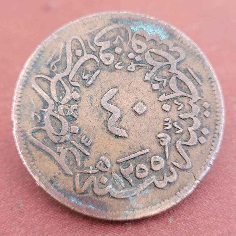 May include: A copper coin with Arabic script and the number "2" in the centre. The coin has a green patina and is slightly worn.