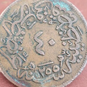 May include: A close-up of a copper coin with Arabic script and the number "3" in the centre. The coin has a green patina and is slightly worn.
