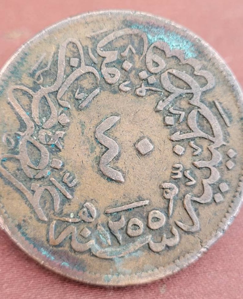 May include: A close-up of a copper coin with Arabic script and the number "3" in the centre. The coin has a green patina and is slightly worn.