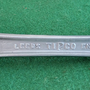 Op de afbeelding: Een zilveren ratelmoersleutel met de tekst "LEEDS TIPCO ENGLAND" op de handgreep.