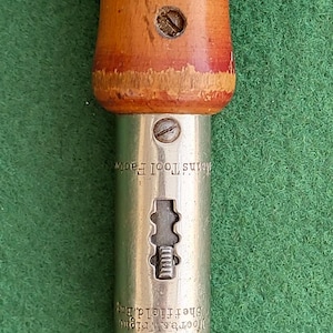 May include: A vintage screwdriver with a wooden handle and a metal shaft. The handle is brown with red and white paint. The metal shaft has the text "Moore's Twisting Sheffield England" and "Mains Tool Facto" engraved on it.