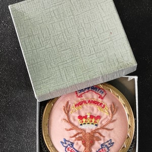 Puede incluir: Un parche redondo, rosa, bordado con un marco dorado. El parche presenta un ciervo rojo con cuernos, una corona dorada y el texto "32nd HIGHLANDERS CUIDICH'N RI'L".