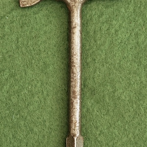 May include: A vintage metal tool featuring a T-shaped design with a weathered, dark gray finish. The head includes a flat, wide blade on one side and a rounded, cylindrical striking end on the other, while the handle terminates in a flat screwdriver tip.