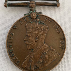 Puede incluir: Una medalla de bronce con un perfil del rey Jorge V, la inscripción "GEORGIVS V REX ET IND: IMP:" y un lazo para una cinta.