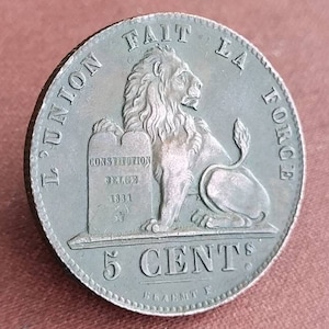 May include: A copper 5 cent coin from Belgium featuring a lion standing on a stone tablet with the inscription "Constitution Belge 1831" and the text "L'Union Fait La Force" around the edge.
