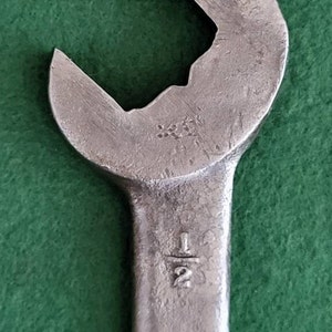 K&ouml;nnte beinhalten: Ein silberner Schraubenschl&uuml;ssel mit einer Gr&ouml;&szlig;enmarkierung von 1/2 Zoll. Der Schraubenschl&uuml;ssel hat einen abgerundeten Kopf und einen langen Griff.